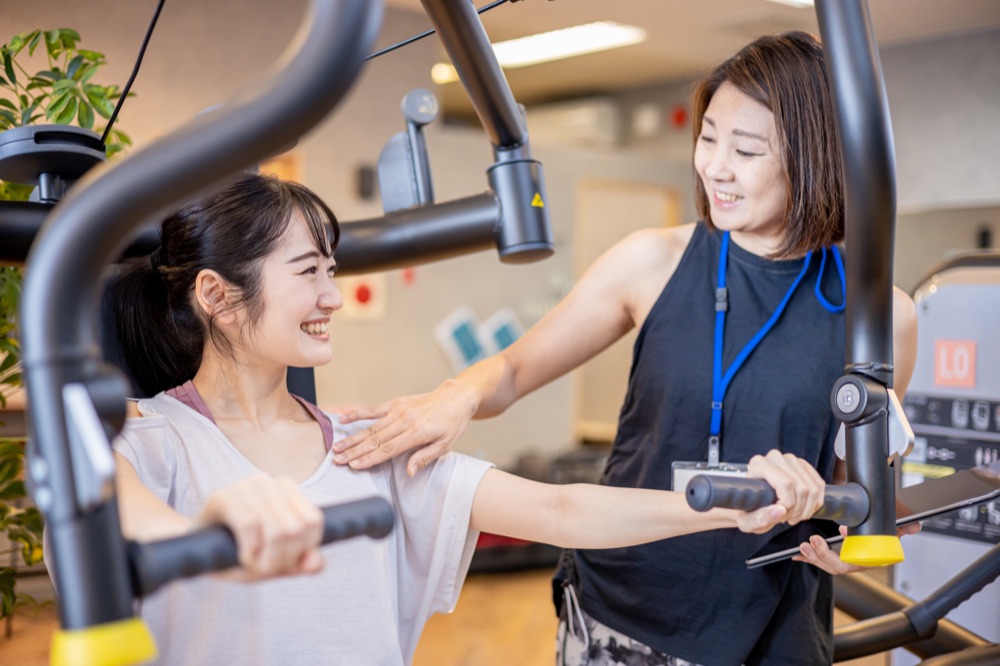 トレーナーに見守られながら、マシンでトレーニングをする女性